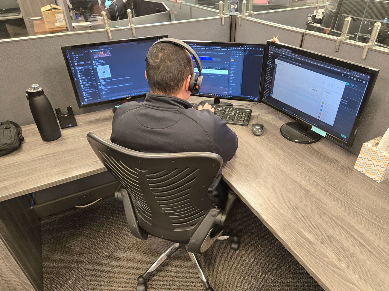 A McNallan technician wearing a headset at a three-monitor workstation in the Brooklyn Park office