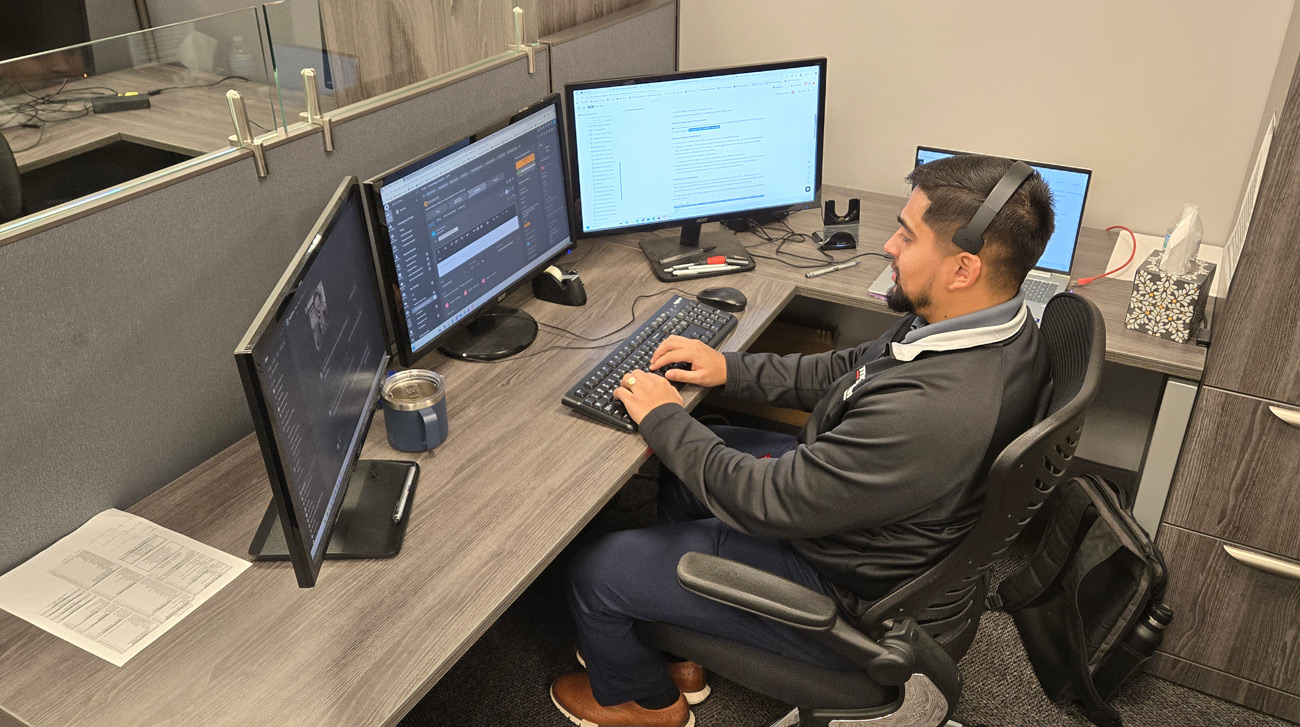 A smiling McNallan technician wearing a headset, working at a multi-monitor desk